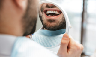 Man’s smile reflected in handheld mirror 