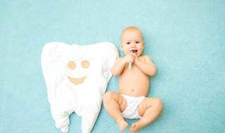 baby with toothbrush in mouth next to tooth pillow
