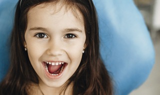 beautiful young girl with brown eyes smiling in dentist’s chair