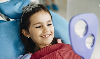 young girl admiring teeth in mirror after fluoride treatment