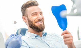 bearded man seeing his new smile in mirror in dental chair 
