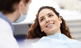 A smiling young woman looking at a dentist while sitting in a dentist’s chair