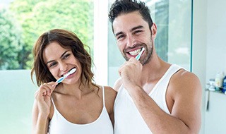 Couple preventing dental emergencies in Burlington by brushing their teeth
