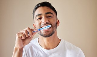 a man brushing his teeth after recovering from tooth extractions