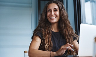 Woman smiling while working on laptop in office