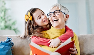 Grandparent and granddaughter smiling while reading book at home