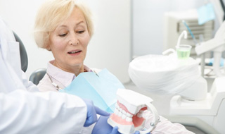 Dentist holding a dental model and explaining implant denture process to patient