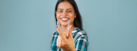 Woman in plaid shirt smiling while holding clear aligners