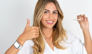 Woman giving thumbs up and holding Invisalign aligner