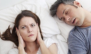 Woman covering her ears next to snoring man