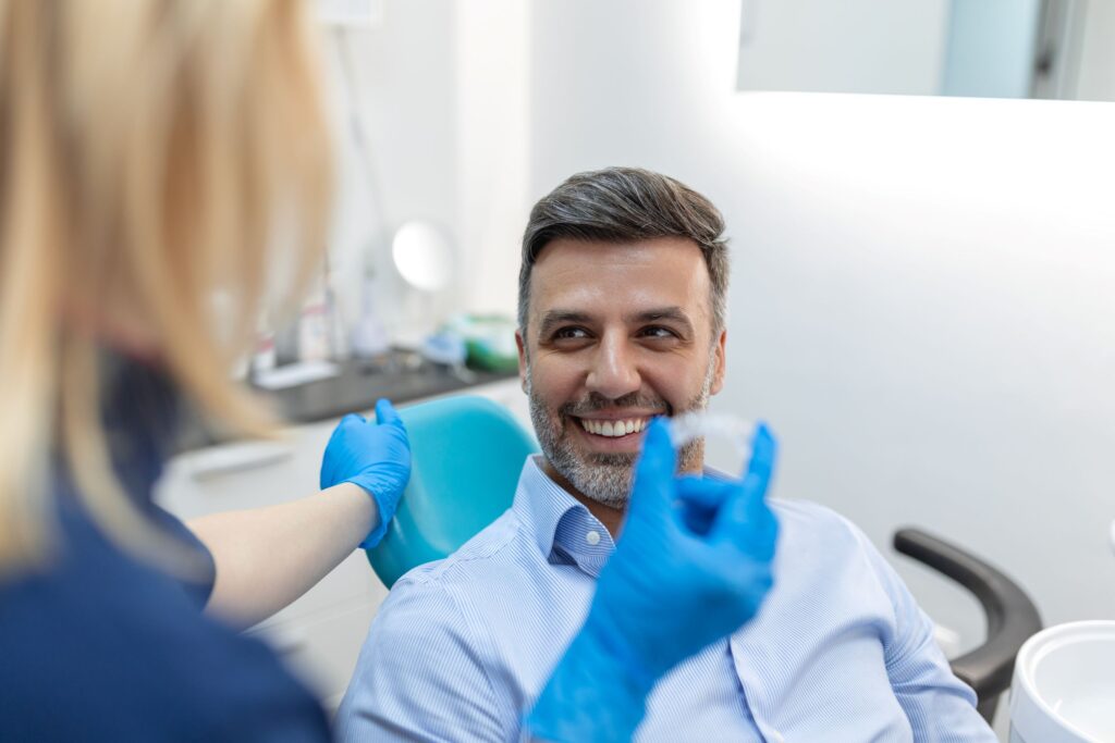 Man in dental chair smiling at dentist holding Invisalign